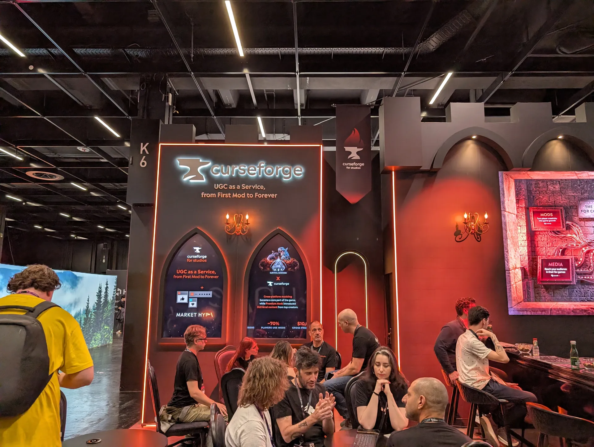 El stand de CurseForge en Gamescom 2026, con visitantes sentados en las mesas bajo el cartel